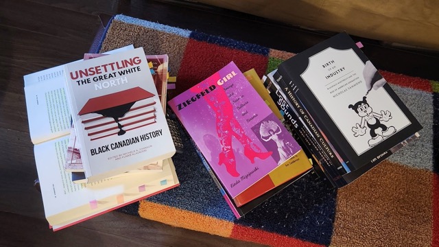 layout of books across a table, titles read 'UNSETTLING THE GREAT WHITE NORTH: BLACK CANADIAN HISTORY," "ZIEGFELD GIRL" and "BIRTH OF THE INDUSTRY"